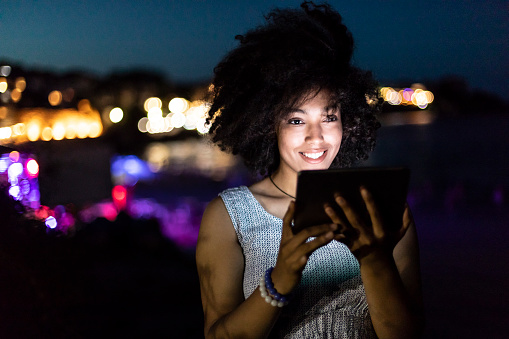 Cheerful african woman using digital tablet on beach at night.