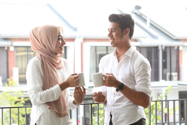 A Young Malay Muslim Couple Having a Drink by a Balcony A young Muslim Malay couple having a drink by a balcony, taking a break from unpacking boxes at their new home. malay couple stock pictures, royalty-free photos & images