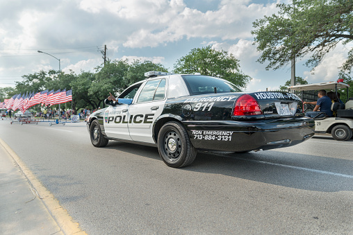 Houston, Texas, USA. 11th May 2013. Houston police car at Houston art car parade with American flags on the background. Policeman points his finger out of the window.