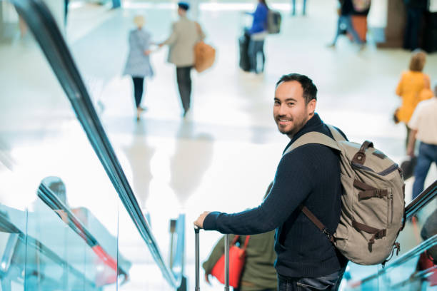 istock Hispanic man looks back while riding escalator with luggage in airport 1065677306