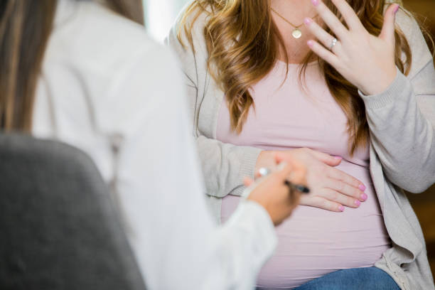 mulher grávida, explicando os sintomas ao médico ou parteira durante a consulta - midwife human pregnancy women multi ethnic group - fotografias e filmes do acervo