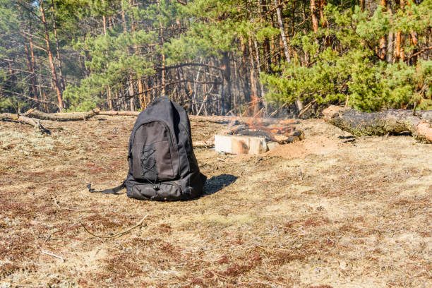 istock Backpack on a ground in a coniferous forest. Bonfire on a background 1065685866