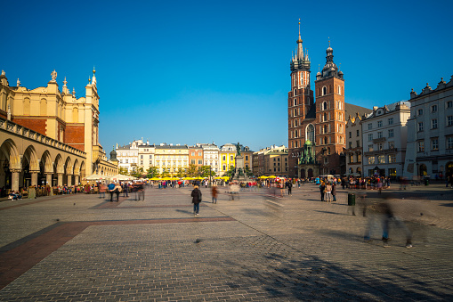 Krakow, Poland - October 22, 2018: Krakow  view showing Sukiennice Cloth or Drapers Hall and St. Mary's Basilica church in Krakow Old town square, building apartments, restaurants, trees and people walking on the street can be seen on the background
