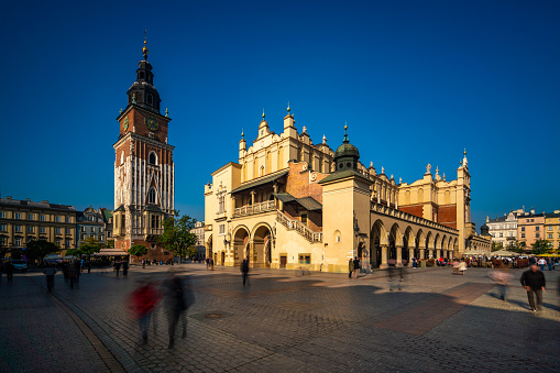 Krakow, Poland - October 22, 2018: Krakow  view showing Sukiennice Cloth or Drapers Hall in the center of the main market in Krakow old town square, building apartments, bell and clock tower,  restaurants on the side of the street and people walking and eating on the street can be seen on the background