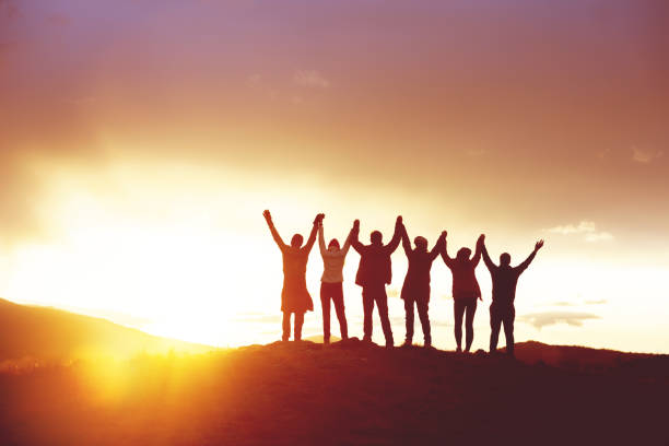 Big group happy people's silhouettes success raised hands Big group of happy friends with raised hands at sunset. People's silhouettes. Unity, success, team or friendship concept sports team stock pictures, royalty-free photos & images