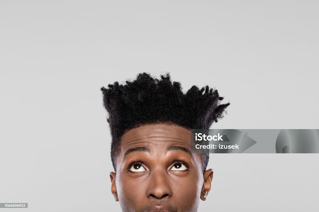 Half face of young african guy looking up Close up of afro american man with looking upwards on gray background. Half face of young guy with funky hairstyle looking at copy space. Halved Stock Photo