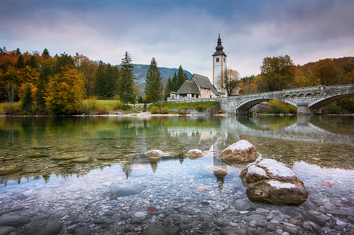 Beautiful landscape of lake Bohinj, Triglav National Park, Julian Alps in Slovenia with church and arch bridge on blue cloudy sky background