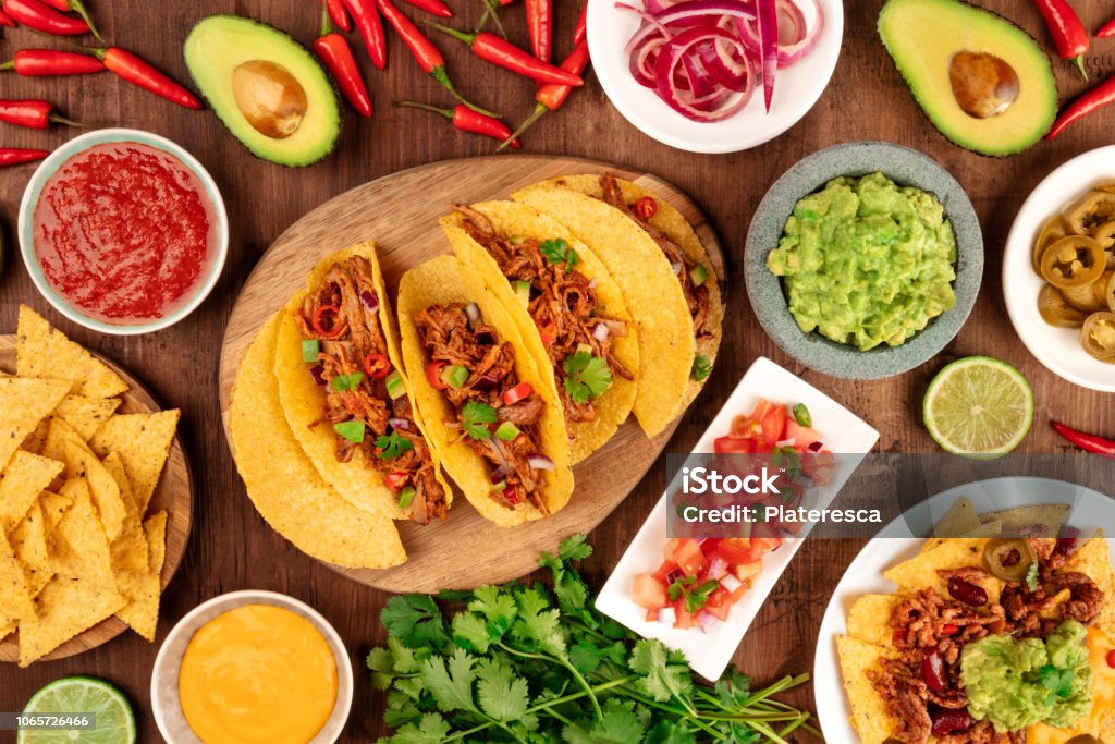 A photo of Mexican food, including tacos, guacamole, pico de gallo, nachos and others, shot from the top with ingredients on a dark rustic wooden background Taco Stock Photo