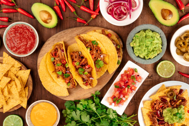 a photo of mexican food, including tacos, guacamole, pico de gallo, nachos and others, shot from the top with ingredients on a dark rustic wooden background - guacamole avocado mexican culture food imagens e fotografias de stock