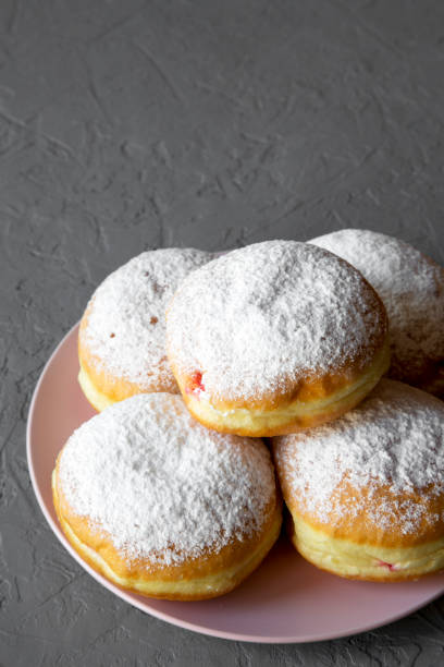 istock Homemade sweet donuts with powdered sugar on pink plate over grey background, side view. Copy space. 1065727702