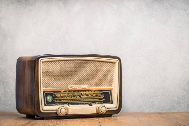 Retro broadcast table radio receiver with green eye light, studio microphone circa 1950 on wooden desk front concrete wall background. Listen music concept. Vintage instagram old style filtered photo stock photo