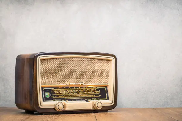 Photo of Retro broadcast table radio receiver with green eye light, studio microphone circa 1950 on wooden desk front concrete wall background. Listen music concept. Vintage instagram old style filtered photo
