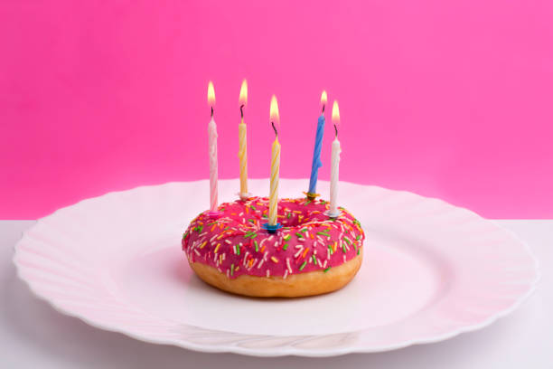 istock Pink donut on white plate like a birthday cake with candles 1065740116