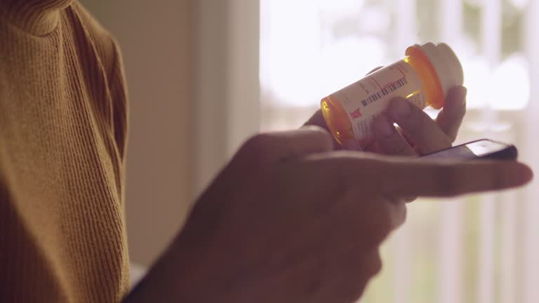 Young asian woman holding pill bottle and talking on mobile phone in bedroom