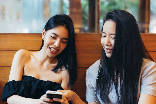 istock Two young attractive Asian women using a mobile phone together at restaurant with happiness and joy 1065746486