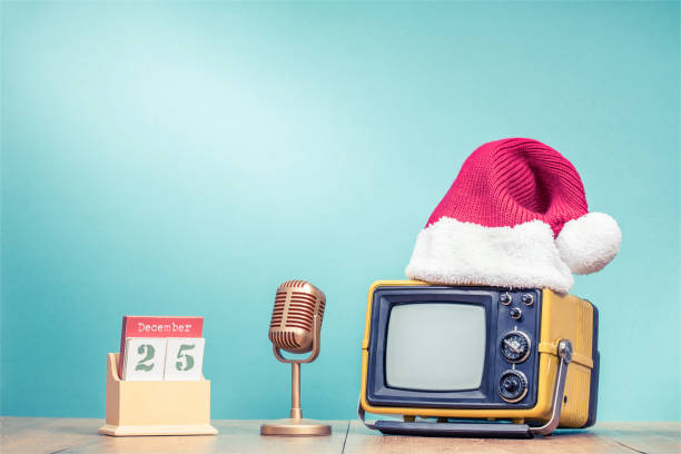 Retro TV in Santa hat, golden microphone and wooden desk calendar with 25 of December date front mint green background. Holidays congratulation in mass media concept. Vintage old style filtered photo retro tv en santa sombrero, micrófono de oro y calendario de escritorio de madera con 25 de diciembre fecha frente menta verde de fondo. felicitación de vacaciones en concepto de medios de comunicación. foto filtrada del viejo estilo de época