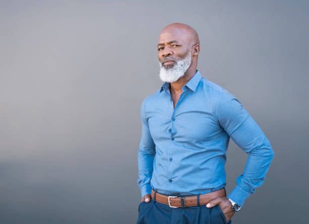 Portrait of confident African American male against gray wall Portrait of confident ceo standing against gray wall. Mature professional is with hands in pockets. three quarter length stock pictures, royalty-free photos & images