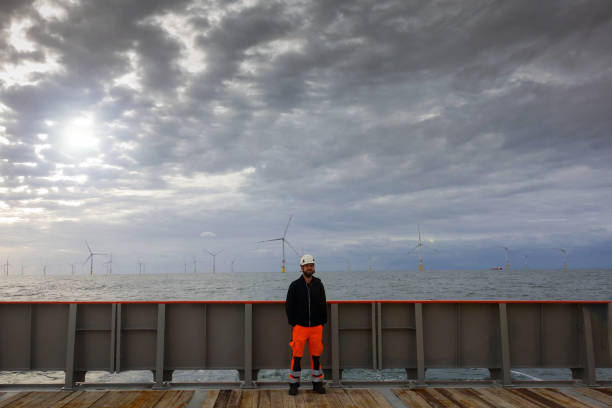 istock Offshore manual worker standing on boat deck with wind-turbines behind him. 1065764544