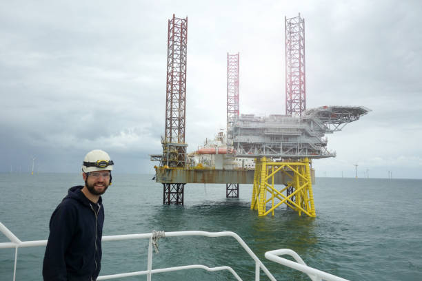 istock Offshore manual worker standing on boat deck with offshore platform and wind-turbines behind him and smiling 1065764616