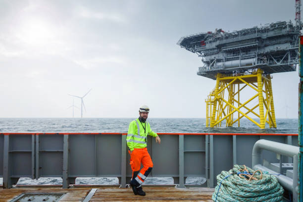 istock Offshore manual worker standing on boat deck with platform and wind-turbines behind him 1065764860