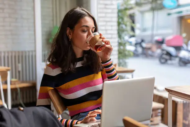 Young Woman Working at her Laptop while Drinking Coffee in a Coffeeshop