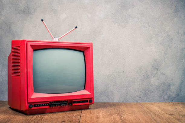 Retro red outdated classic TV receiver on table front textured concrete wall background. Television broadcasting concept. Vintage old style filtered photo