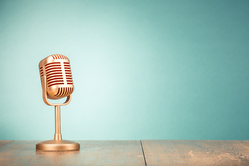 Retro golden microphone for press conference or interview on table front gradient mint green background. Vintage old style filtered photo