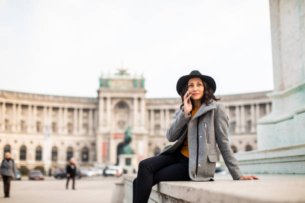 I call you from Vienna Woman talking on mobile phone while sitting on concrete in front of famous building in Vienna, Heldenplatz the hofburg complex stock pictures, royalty-free photos & images