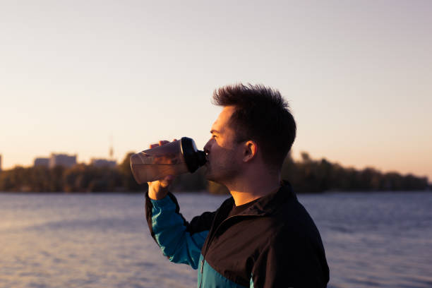istock Closeup of a handsome man drinking water outside after training at sunset 1065799976