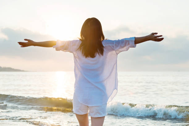 istock Young woman standing on beach with arms outstretched 1065816270