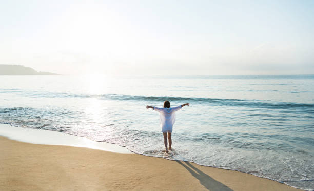 istock Young woman standing on beach with arms outstretched 1065816454