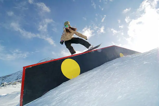 young snowboarder woman riding on jibbing box 