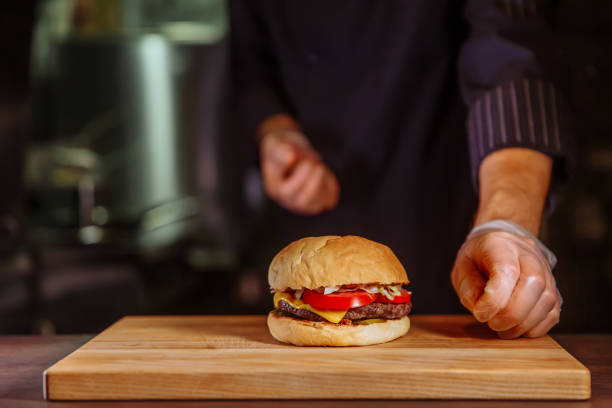 chef che mette il panino in cima, fa un hamburger di manzo per l'ordine del cliente - white food and drink industry hamburger cheeseburger foto e immagini stock