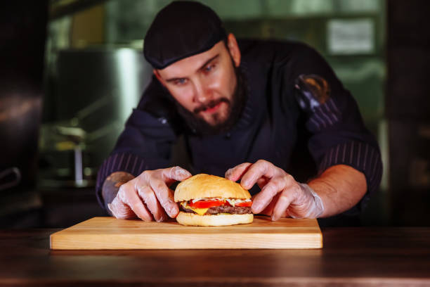 chef, mettre le pain sur le dessus, il faire un hamburger de boeuf pour la commande du client - white food and drink industry hamburger cheeseburger photos et images de collection