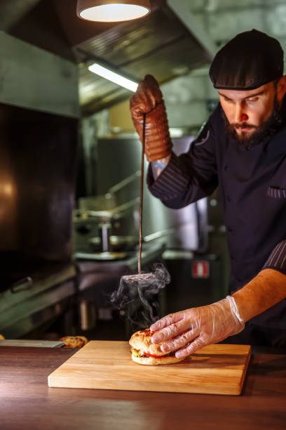 chef che mette il panino in cima, fa un hamburger di manzo per l'ordine del cliente - white food and drink industry hamburger cheeseburger foto e immagini stock