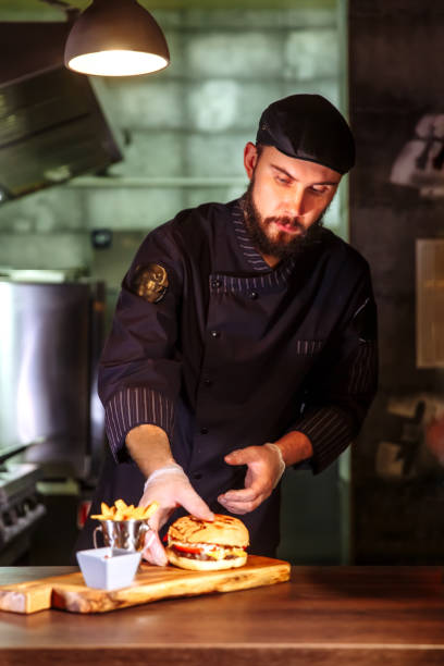 chef che mette il panino in cima, fa un hamburger di manzo per l'ordine del cliente - white food and drink industry hamburger cheeseburger foto e immagini stock