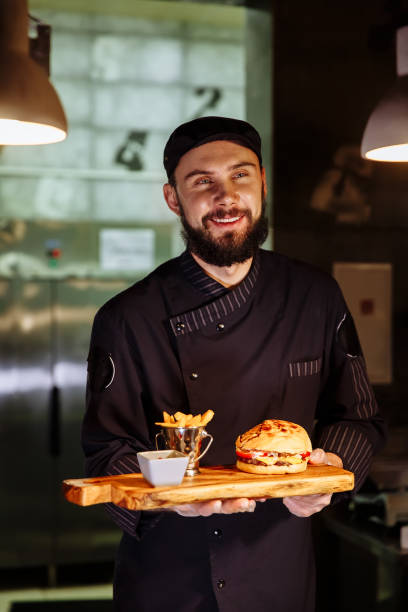 istock Smiling master chef in uniform looking at camera, holding plate with served burger 1065820082