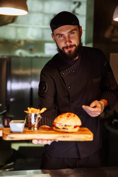 istock Smiling master chef in uniform looking at camera, holding plate with served burger 1065820084