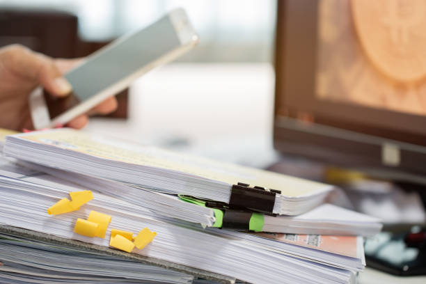 istock Documents stack of paperwork and report files on busy overwork desk with blur businessman hands working using apps for searching information in smartphone. Business concept 1065832380