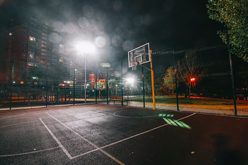 Illuminated basketball playground with red pavement, modern new basketball net and lens flares on background.