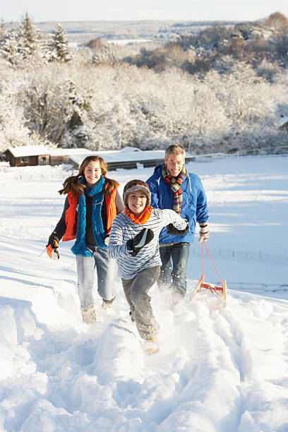 Father And Children Pulling Sledge Up Snowy Hill stock photo