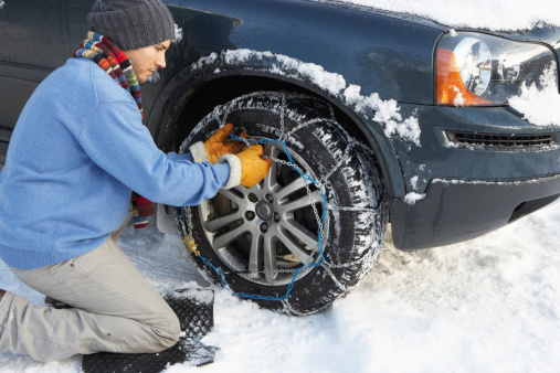 Man Putting Snow Chains Onto Tyre Of Car on his knees