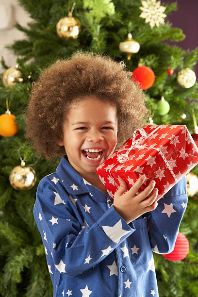 istock Young Boy Holding Gift In Front Of Christmas Tree 106586111