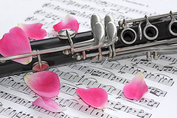 A close-up of an old clarinet resting on music.  A few rose petals are scattered around.  