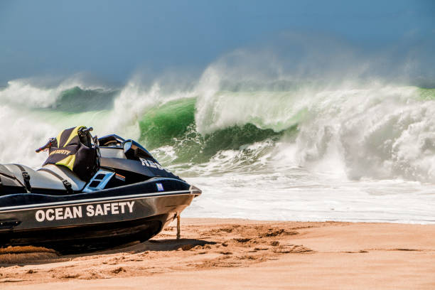 Lifeguard jetski sits on the golden sandy beach of hawaii as a big wave crashes in the background.