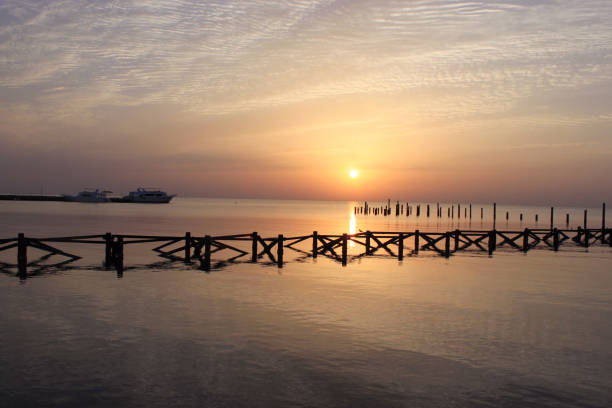 golden sunrise on the sea. wooden piles of old destroyed pier sticking out of the water. the ship departs from the marina in the distance. - safaga imagens e fotografias de stock