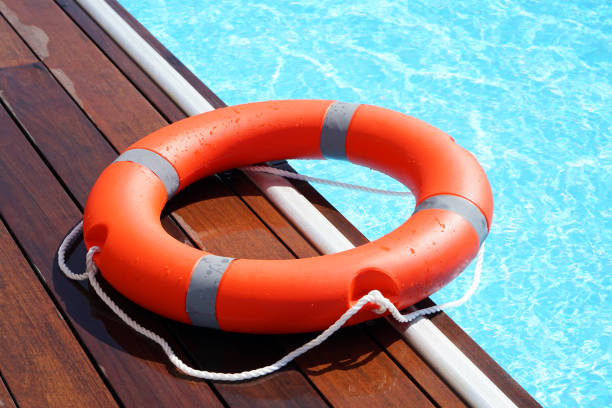 Red lifebuoy pool ring float The red life ring lies on the wooden floor of the swimming pool. Life cycle, floating above the sunny blue water. Ring of life in the pool buoy stock pictures, royalty-free photos & images