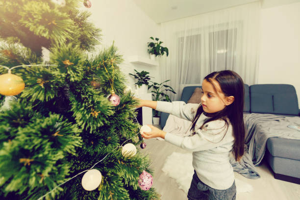 Little girl decorating Christmas tree on bright background