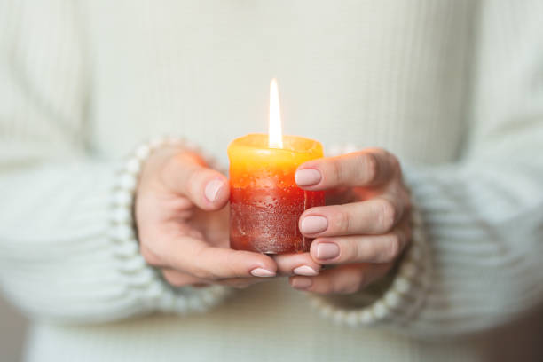 istock A woman in a light warm woolen keeps a burning candle in her hands, copy space, selective focus. Christmas, new year holiday concept 1065917336