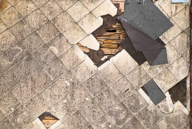 Photo of Old damaged roof of asbestos shingles requiring repair. Dirty beams and torn waterproofing of roofing material.